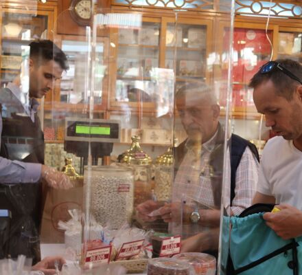 zwei Verkäufer links und zwei Kunden rechts, getrennt durch Glasscheiben in einem Süsswarenladen